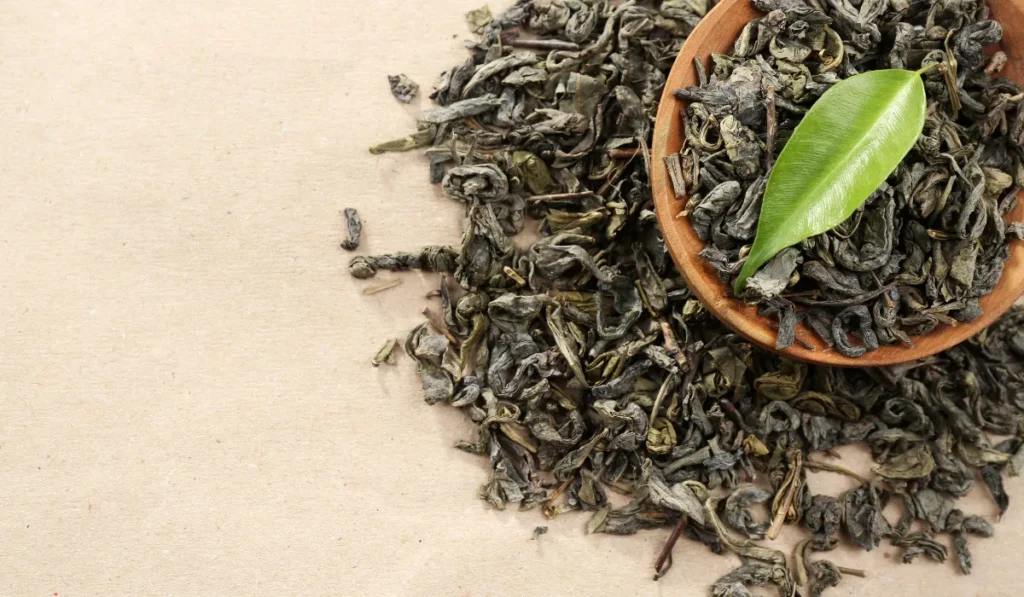 06 Natural Ways to Get Rid of Pimples 2024 4 Close-up of a green tea leaf on top of dried tea leaves in a wooden bowl, highlighting natural antioxidants beneficial for health and skincare.