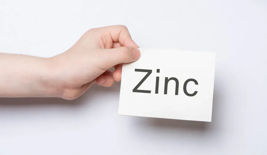06 Natural Ways to Get Rid of Pimples 2024 7 A person's hand holding a white card with "Zinc" written on it, symbolizing the importance of minerals in health or skincare.