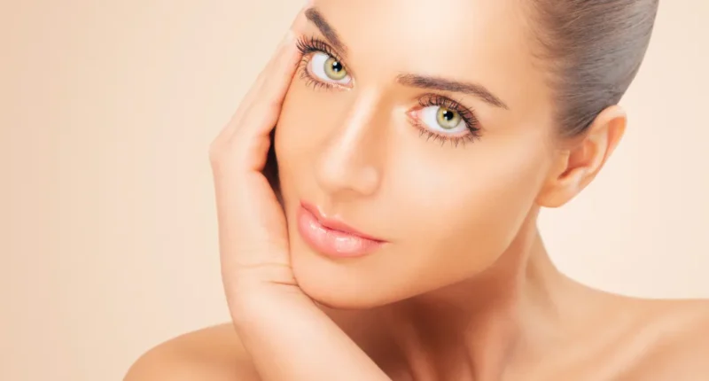 Portrait of a woman with glowing skin gently touching her face, exemplifying refined makeup techniques for a natural and fresh look, ideal for everyday beauty inspiration.