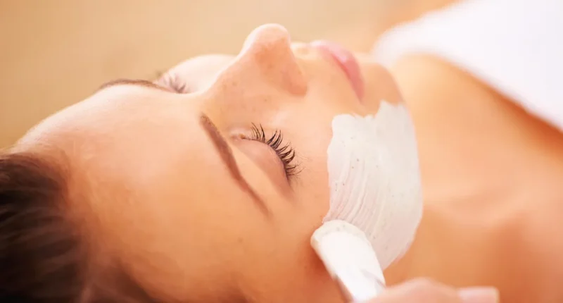 A serene woman with a facial mask being applied in a spa setting, highlighting a moment of relaxation and skincare routine.