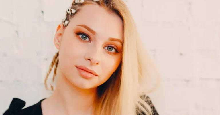 Portrait of a young woman with a side braid adorned with white flowers, her blonde hair contrasted against a light, textured background, highlighting a fresh and youthful look