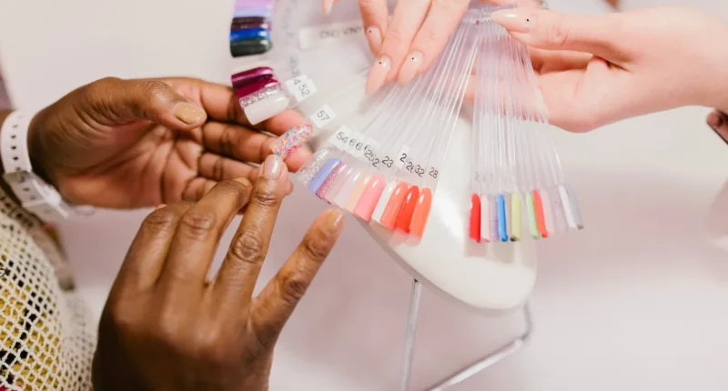 A detailed view of a nail color consultation, with a customer and a manicurist comparing nail color samples against the customer's tan skin to find the perfect shade, showcasing a variety of vibrant and pastel colors.