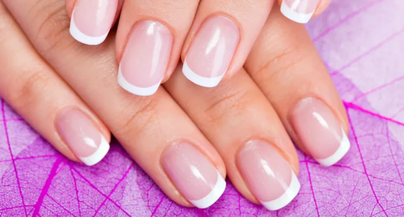A close-up view of well-manicured hands showcasing classic French nails with pristine white tips and a glossy nude pink base, set against a vibrant purple leaf-patterned background, embodying timeless elegance with a pop of color.