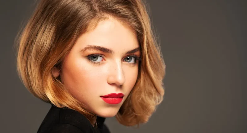 A young woman with a subtle 'Old Money' bob haircut exudes charm and class, her blonde hair with darker roots styled in a sleek, inward curl