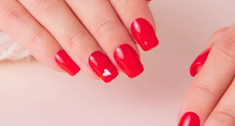 Vibrant red nails with a glossy finish featuring a single, delicate white heart as an accent on one finger, embodying a simple yet powerful expression of love for Valentine's Day.